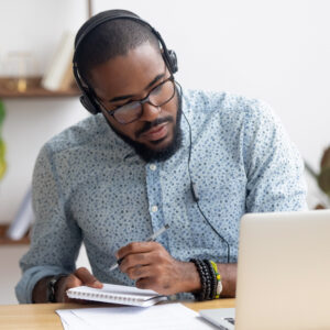 Focused,African,Business,Man,In,Headphones,Writing,Notes,In,Notebook